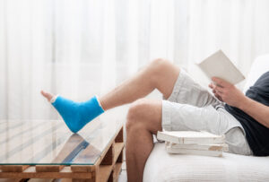 Un hombre con una pierna rota y enyesada se sienta en casa y lee libros.